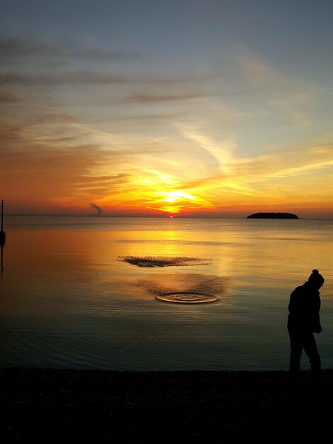 Silhouette person standing at beach against sky during sunset