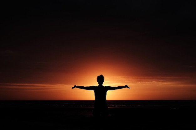 Photo silhouette of person standing on beach at sunset