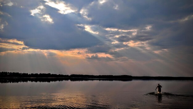 Silhouette person standing by lake against sky during sunset