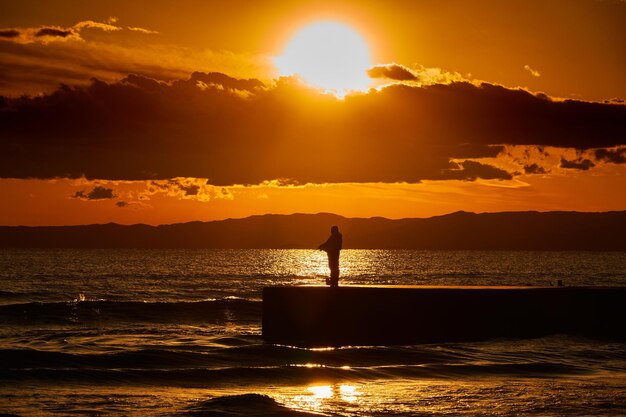 Silhouette person standing by sea against sky during sunset