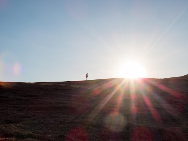 Foto silhouette di una persona in piedi su una collina contro il sole brillante durante il tramonto