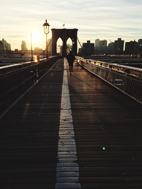 Photo silhouette person walking at brooklyn bridge against sky during sunset