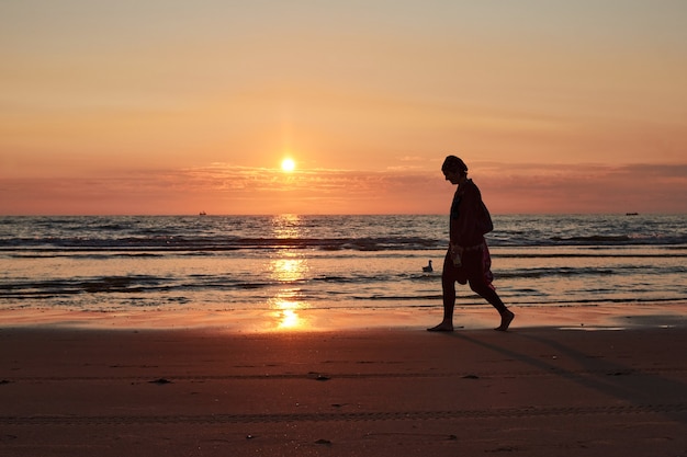 夕暮れ時の海岸を歩く人のシルエット