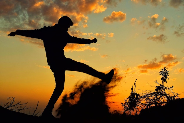 silhouette person with arms outstretched against sky during sunset