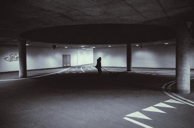 Silhouette person with dog standing under parking garage