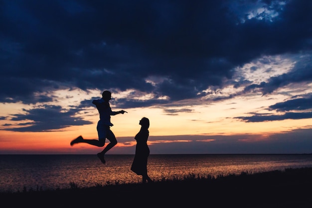 美しい夕日の空と海を背景に恋をしているカップルのシルエット写真。男は高くジャンプした。