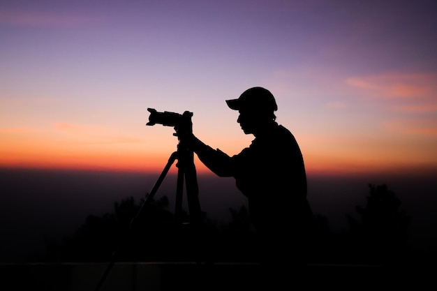 Silhouette di un fotografo con treppiede giovane uomo indiano che scatta foto con la sua macchina fotografica