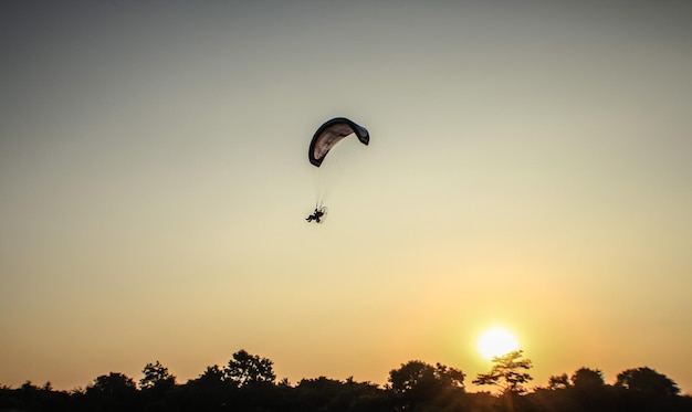 Silhouette picture of the Paramotor is flying through soft sunlight sunset sky