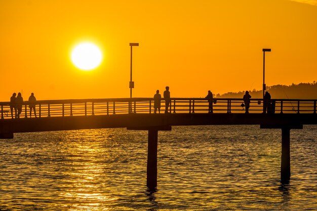 Silhouette pier over sea against orange sky