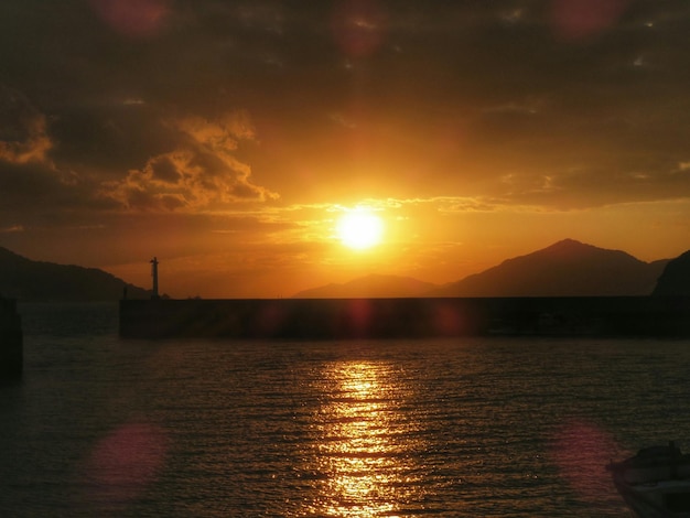 silhouette pier on sea against orange sky
