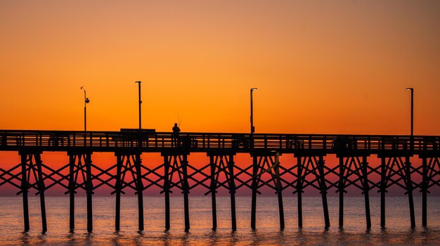 Silhouette pier over sea against romantic sky at sunset