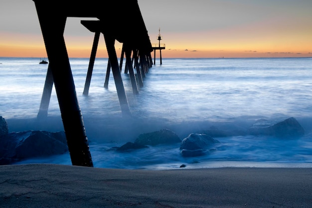 Photo silhouette of pier on sea during sunset