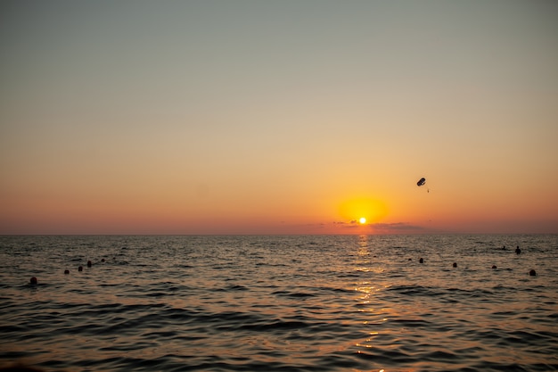 素晴らしいオレンジ色の夕焼け空に対して海の上空を飛ぶ動力を与えられたパラグライダーのシルエット。