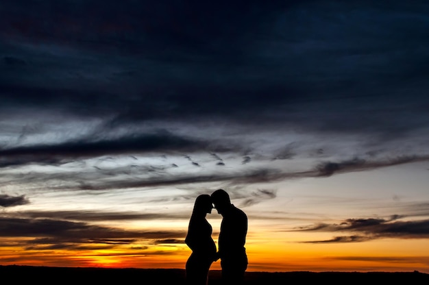 Silhouette of pregnant couple in love at sunset