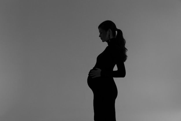 Silhouette of a pregnant girl in a black dress on the background