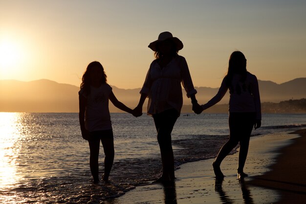 silhouette of pregnant mother and daughters on the beach at sunset