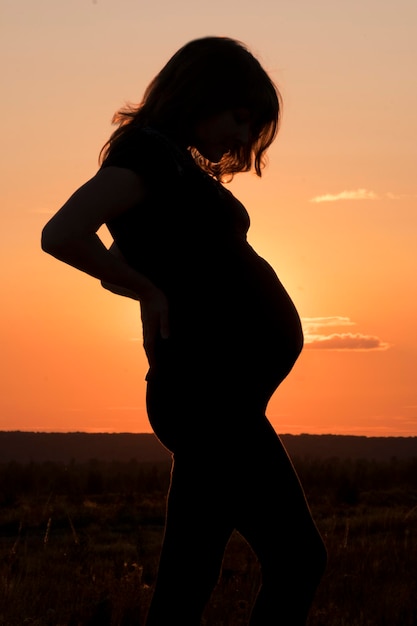 Silhouette of a pregnant woman against the sunset sky