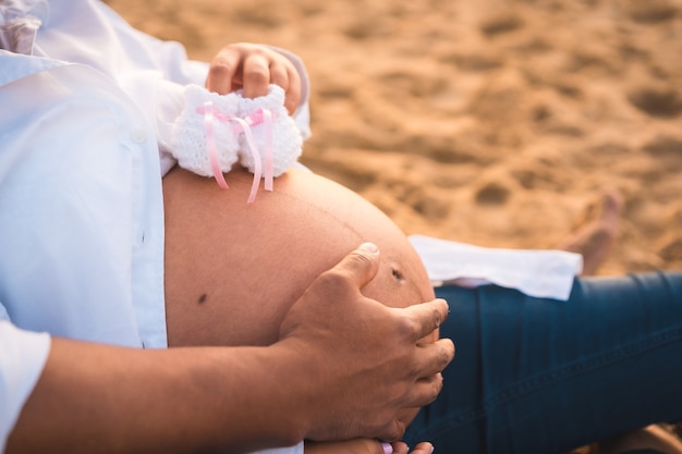 Silhouette of a pregnant woman in a white dress sitting on the beach, pregnant session of a new pregnancy