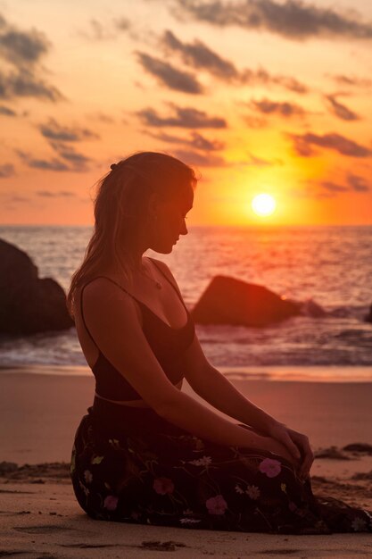 夏休みに海のビーチで夕日を背景に海のビーチに座っているシルエットかなりロマンチックな女性