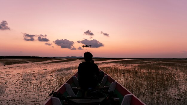 シルエットプロの男性がボートでドローンを制御美しい空の夕日