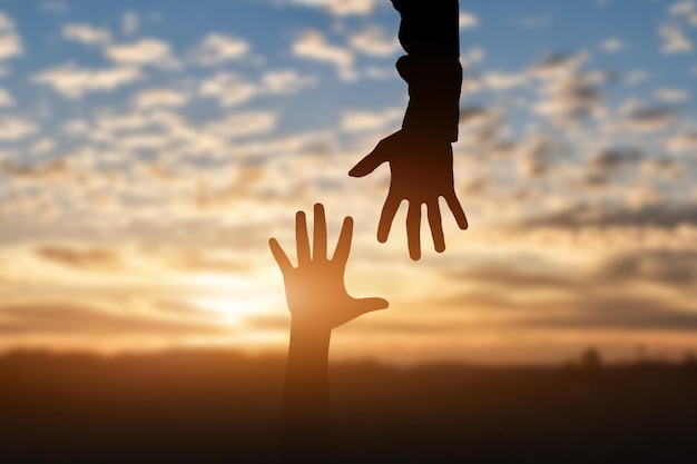 Foto silhouette di raggiungere dando una mano di aiuto speranza e sostenere l'un l'altro sullo sfondo del tramonto concetto di aiuto