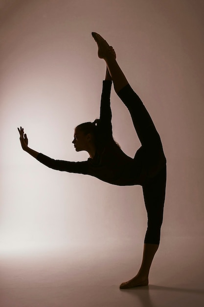 the silhouette of a rhythmic gymnastics girl in a bodysuit shows an exercise in vertical splits