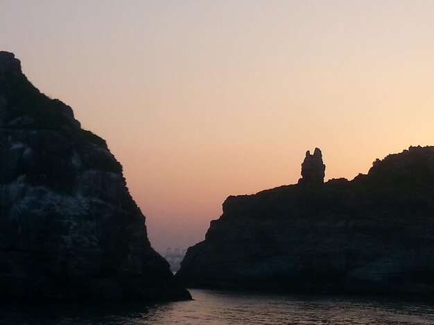 Silhouette rock formations by sea against clear sky