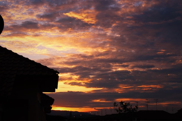 silhouette roof against cloudy orange sky at dusk