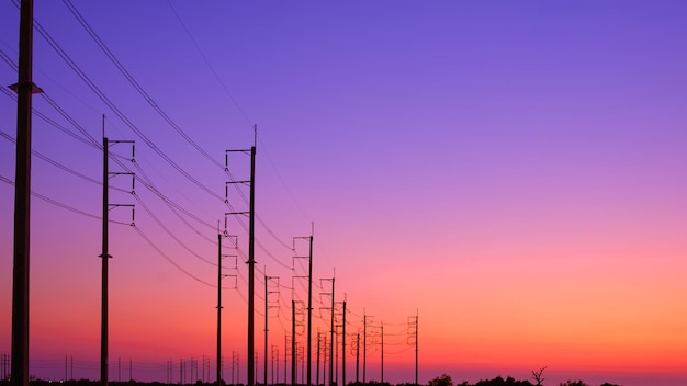 写真 カラフルな夕暮れの空に照らされた田舎の道路のケーブルラインの電柱のシルエット列