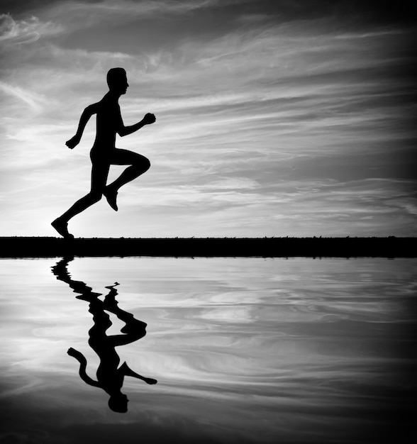 Silhouette of running man against sky. Silhouette of man running at sunset. Water reflection. Black and White. Element of design.