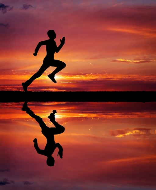 Silhouette of running man on sunset fiery background. Silhouette of man running at sunset. Water reflection. Element of design.