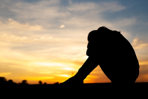 Silhouette of sad and depressed women sitting at walkway of park with sunset