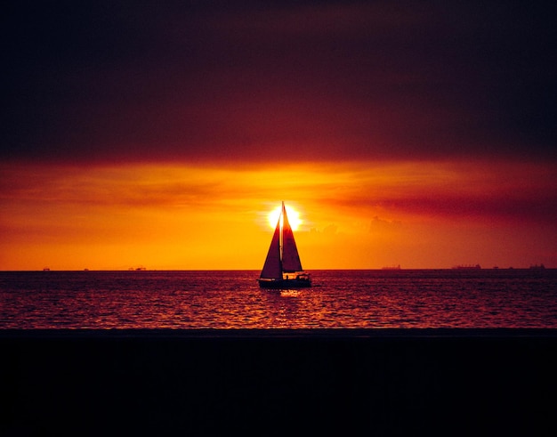写真 夕暮れの空に向かって海を航海するシルエットの帆船