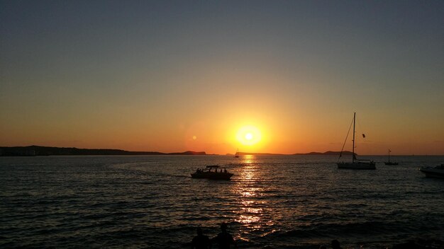 Силуэт парусной лодки, плавающей на море на фоне ясного неба во время захода солнца