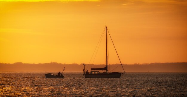 Silhouette sailboat sailing on sea against romantic sky at sunset