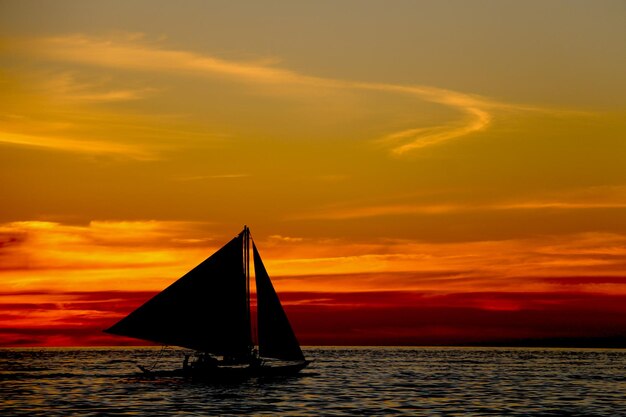 Silhouette sailboat sailing on sea against sky during sunset