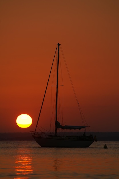 Silhouette sailboat on sea against orange sky