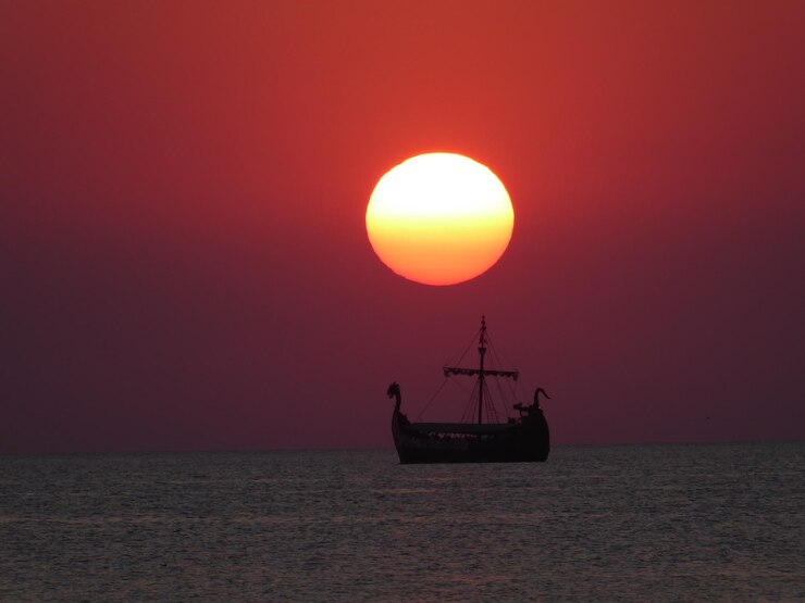 Photo 夕暮れの空に照らされた海のシルエットの帆船