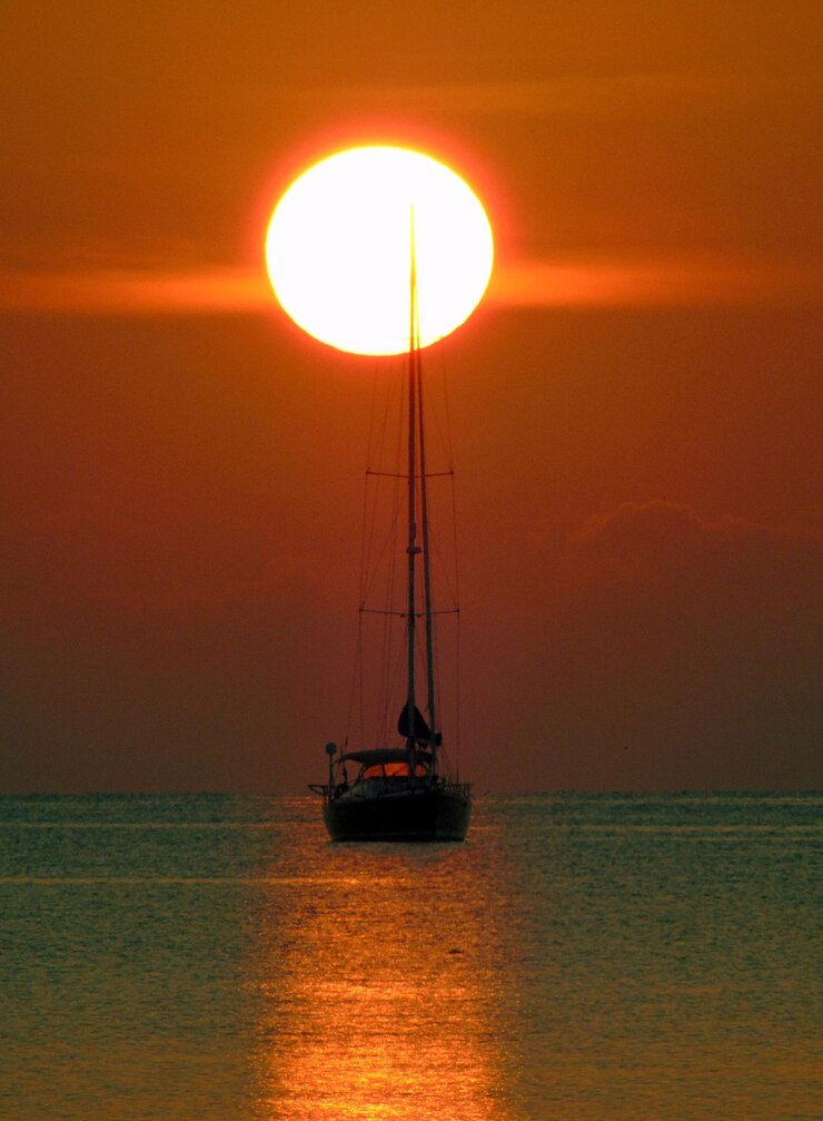 Photo 夕暮れの空に照らされた海のシルエットの帆船