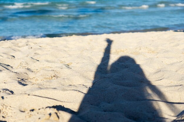 髪を風になびかせ、海と水の波に腕を上げた女性の浜辺の砂の上のシルエット