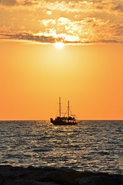 写真 夕暮れの空と対照的に海に浮かぶ船のシルエット