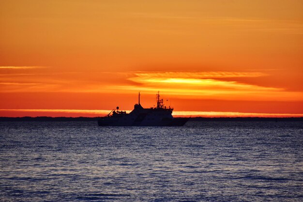 Silhouette ship in sea against orange sky