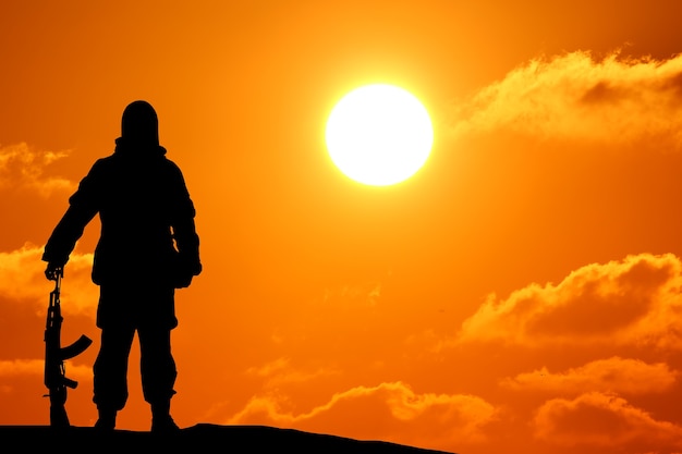 Silhouette shot of soldier holding gun with colorful sky and mountain in background