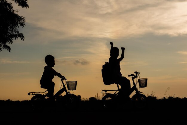 Foto silhouette fratelli in bicicletta su terra contro il cielo durante il tramonto