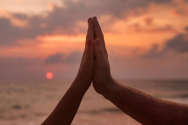 Silhouette sign hands of couple are lovely together at sunset\
of through woman and man hands in together sign shape with sunrise\
and sea ocean background