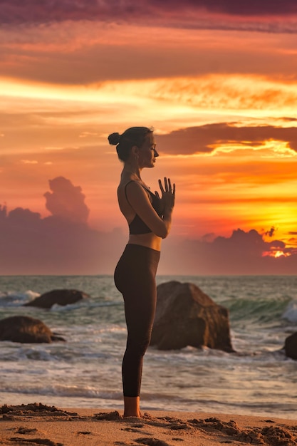 Silhouette slim woman does yoga on tropical sea coast or ocean beach outdoors at sunset