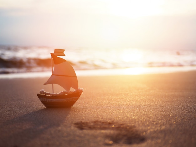 Silhouette small boat toy on sand at sunset beach.