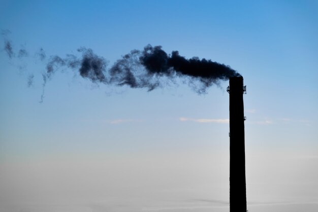 Photo a silhouette of a smoking chimney with a sunset sky in the background