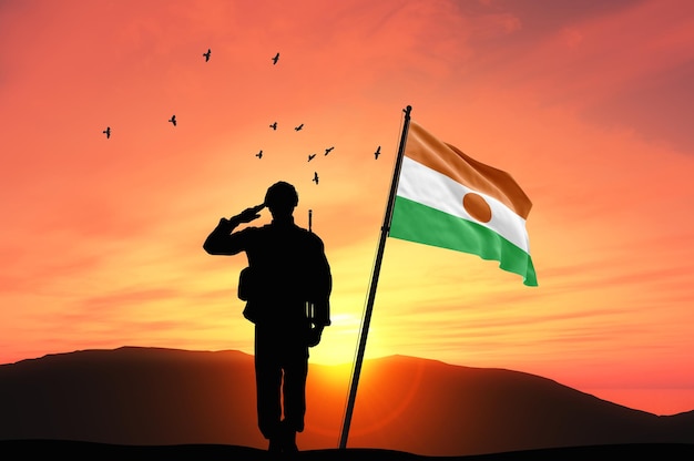 silhouette of a soldier with the niger flag stands against the background of sunset or sunrise