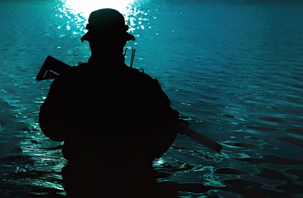 Silhouette of special forces with rifle in action during river\
raid in the jungle waist deep in the water. front view, half\
length